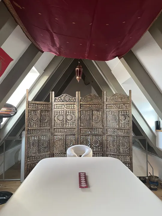 Massageliege vor geschnitztem Paravent im Massageraum in Landshut